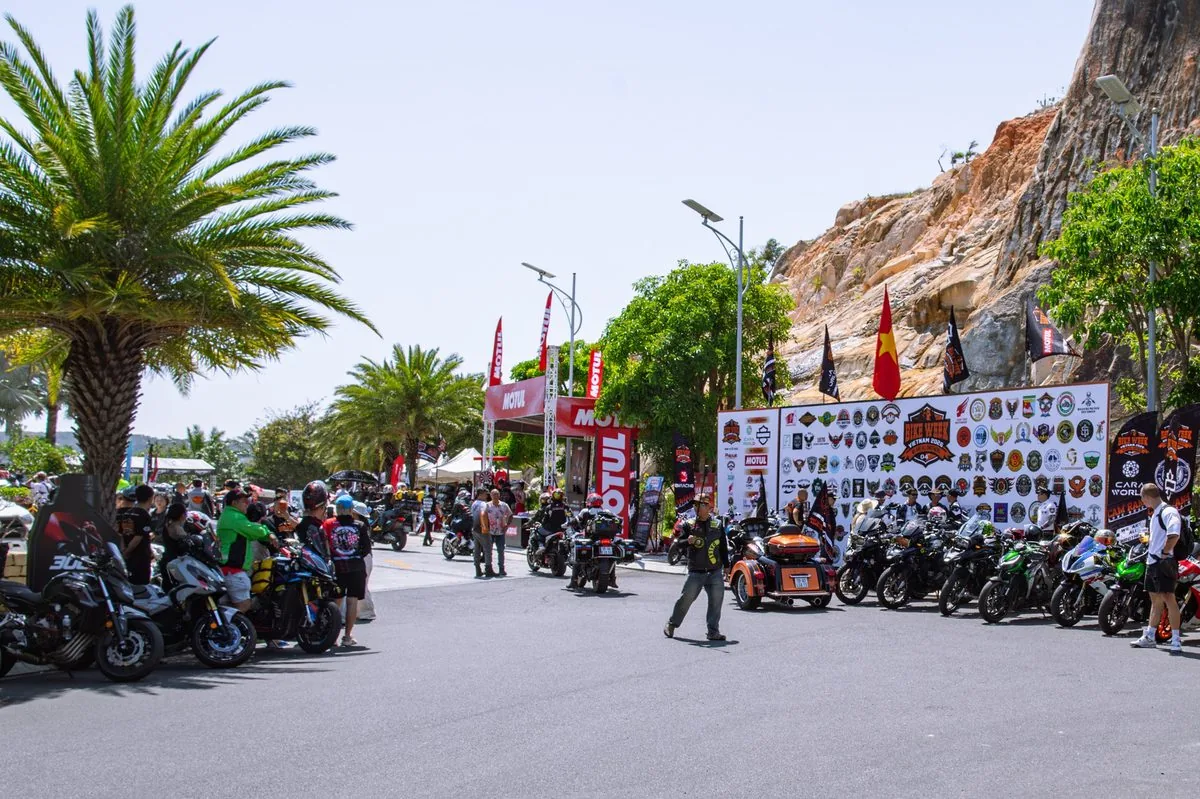 Biker tập trung tại khu vực sự kiện dưới chân núi đá với backdrop logo các câu lạc bộ mô tô Bike Week 2026 Biker tập trung tại khu vực sự kiện dưới chân núi đá với backdrop logo các câu lạc bộ mô tô Bike Week 2026