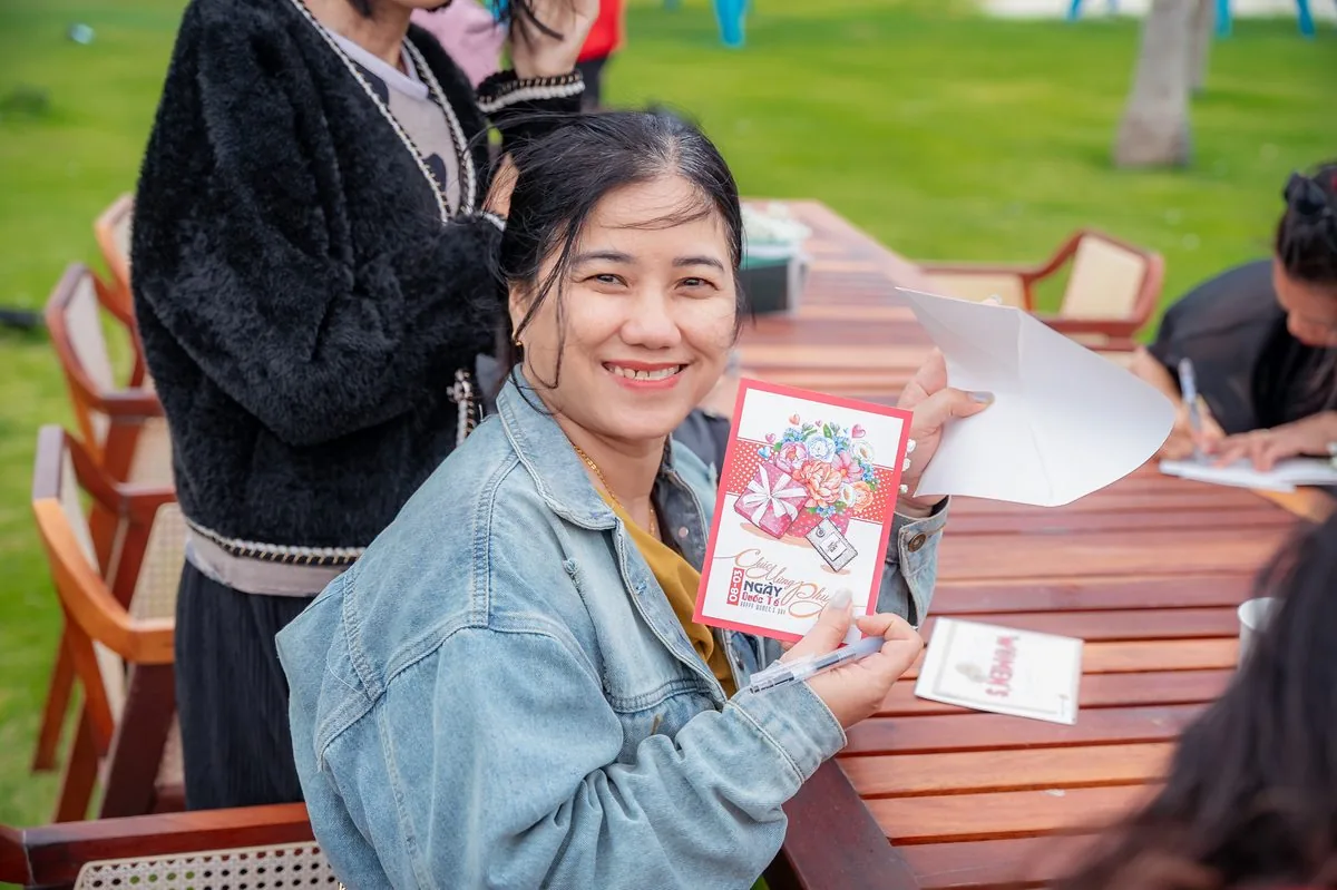 Phụ nữ mỉm cười khoe thiệp chúc mừng ngày 8 tháng 3 tại bàn ngoài trời CaraWorld Cam Ranh